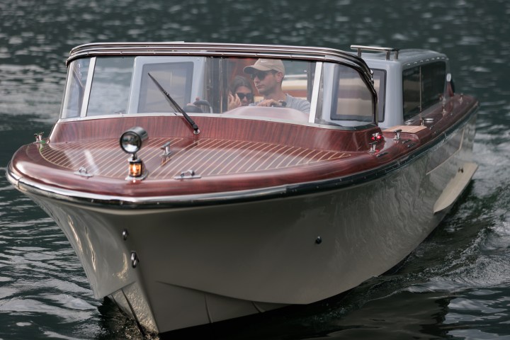 Man driving a sleek, wooden boat on a calm body of water.
