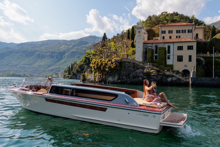 Couple on a boat in a lake, villa and mountains in the background.