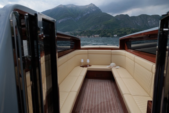 Luxury boat interior with beige seating, wine glasses, and mountains in the background.