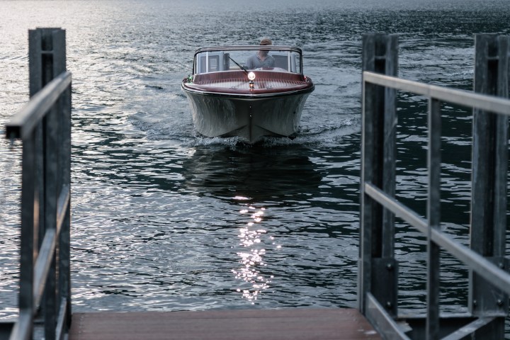 Person driving a small boat approaching a dock on calm water at sunset.