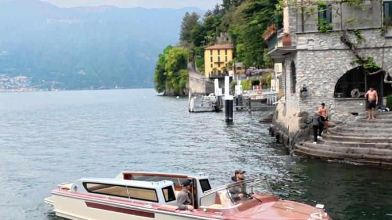 Boat on lake near shore with buildings and trees.
