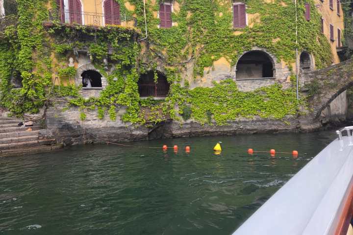 Ivy-covered building by water with arches and buoys floating nearby.