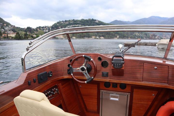 View from wooden motorboat cockpit on a calm lake with hills in the background.