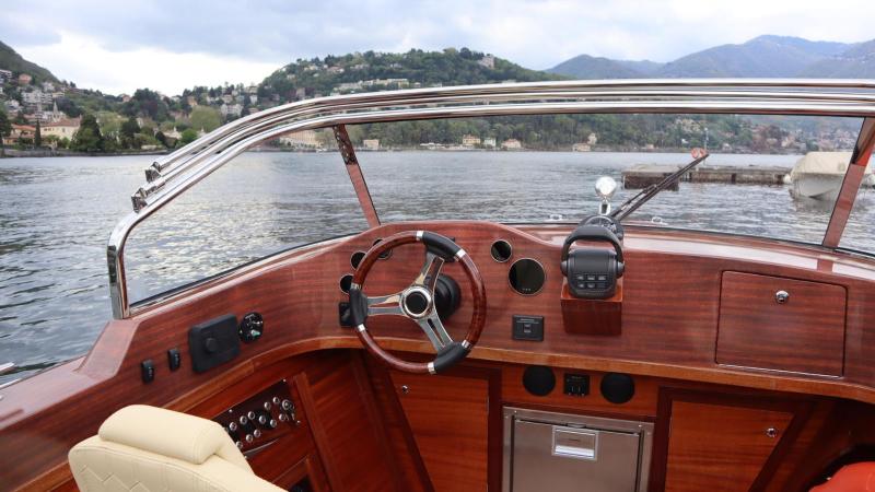 View from wooden motorboat cockpit on a calm lake with hills in the background.
