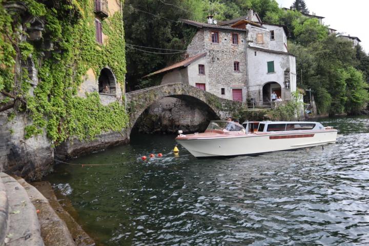 Boat on lake near stone houses and arched bridge.