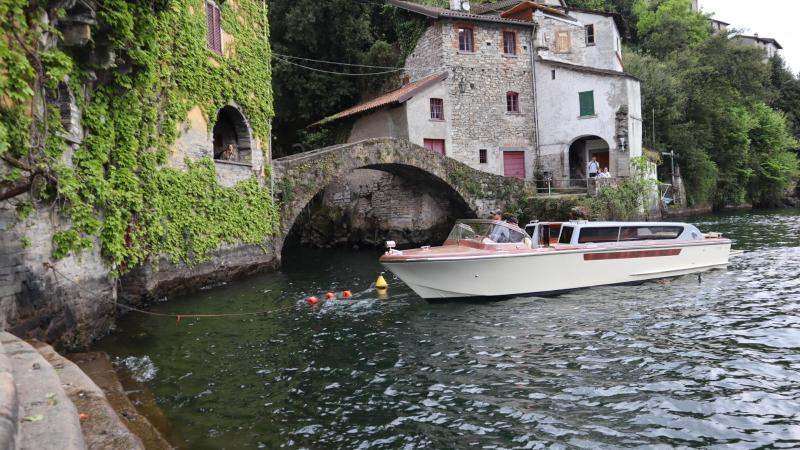 Boat on lake near stone houses and arched bridge.